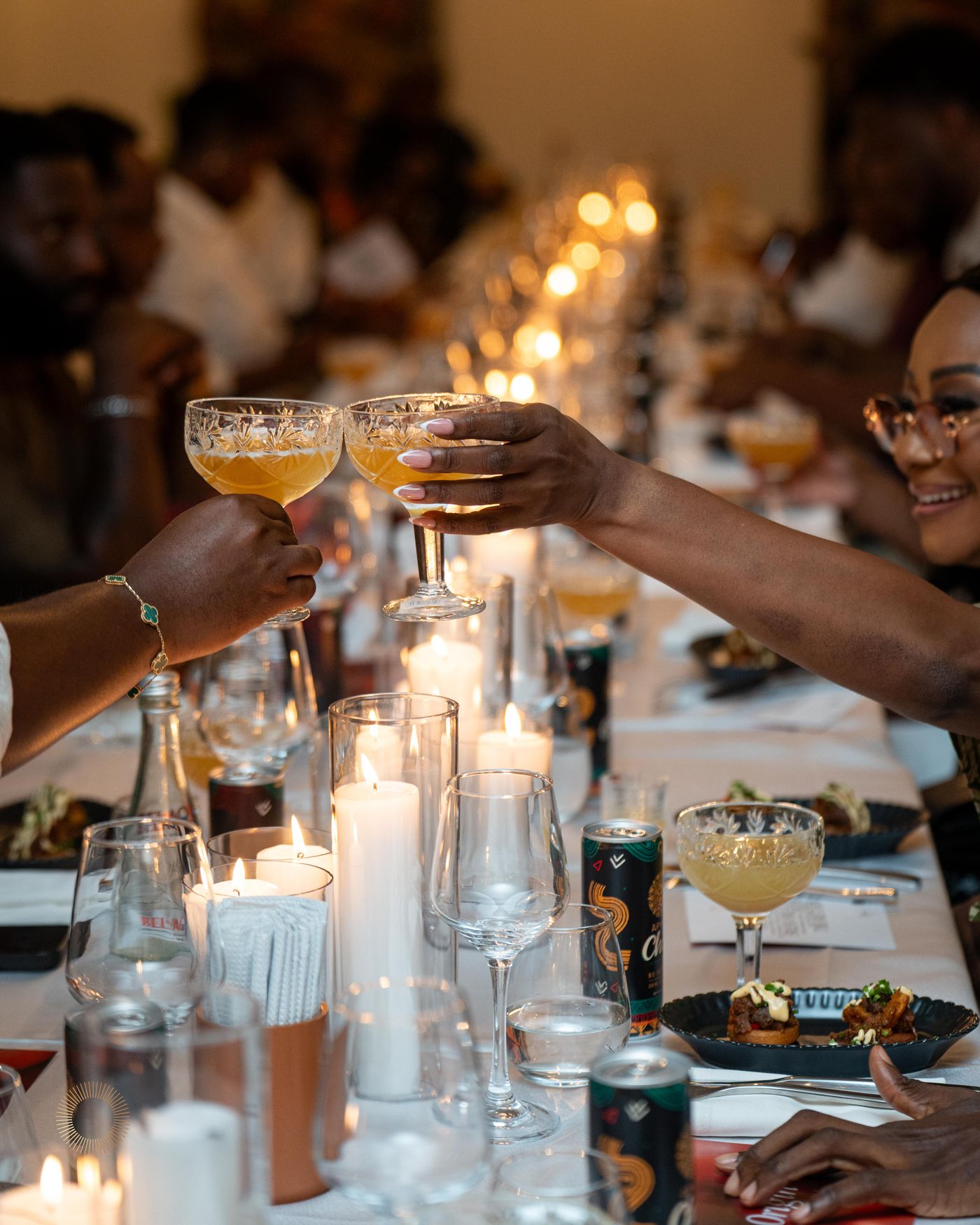 Two hands clinking Aphro cocktail glasses across a dinner table